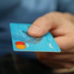 A hand reaching out and handing out a debit card with their thumb covering the card numbers.