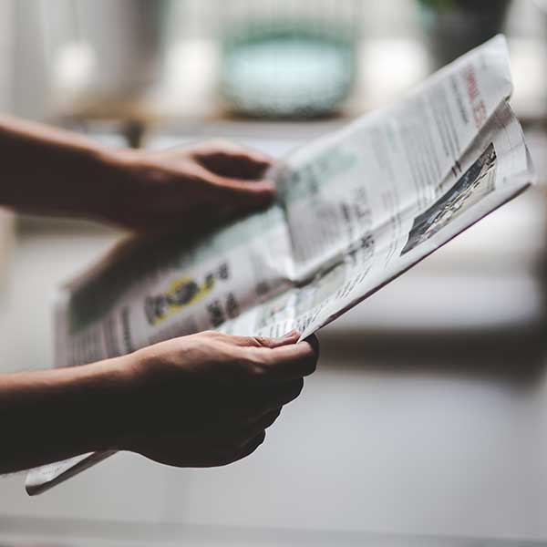Hands holding a newspaper in a dark room with shadows covering their arms.
