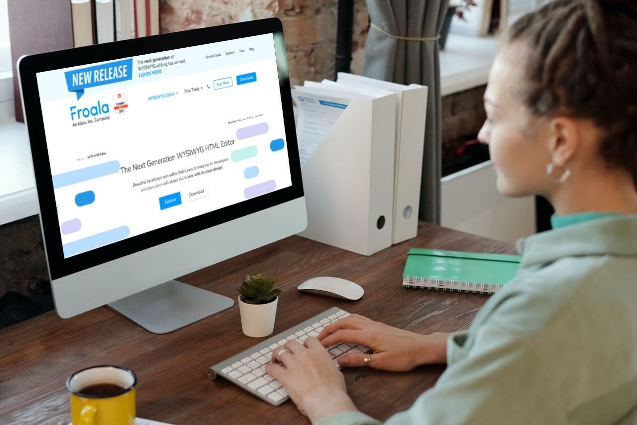 A woman working on an iMac displaying the Froala WYSIWYG HTML editor's website.