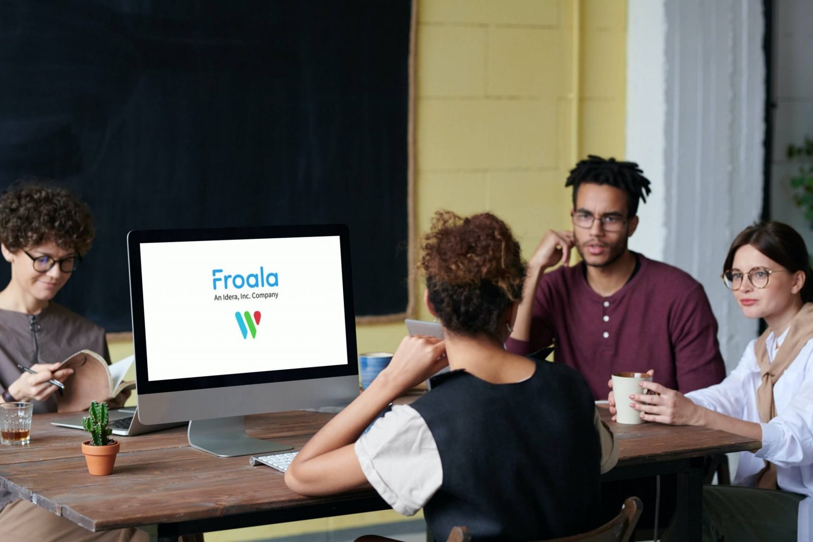 A group of professionals discussing around a computer with Froala's logo on the screen.