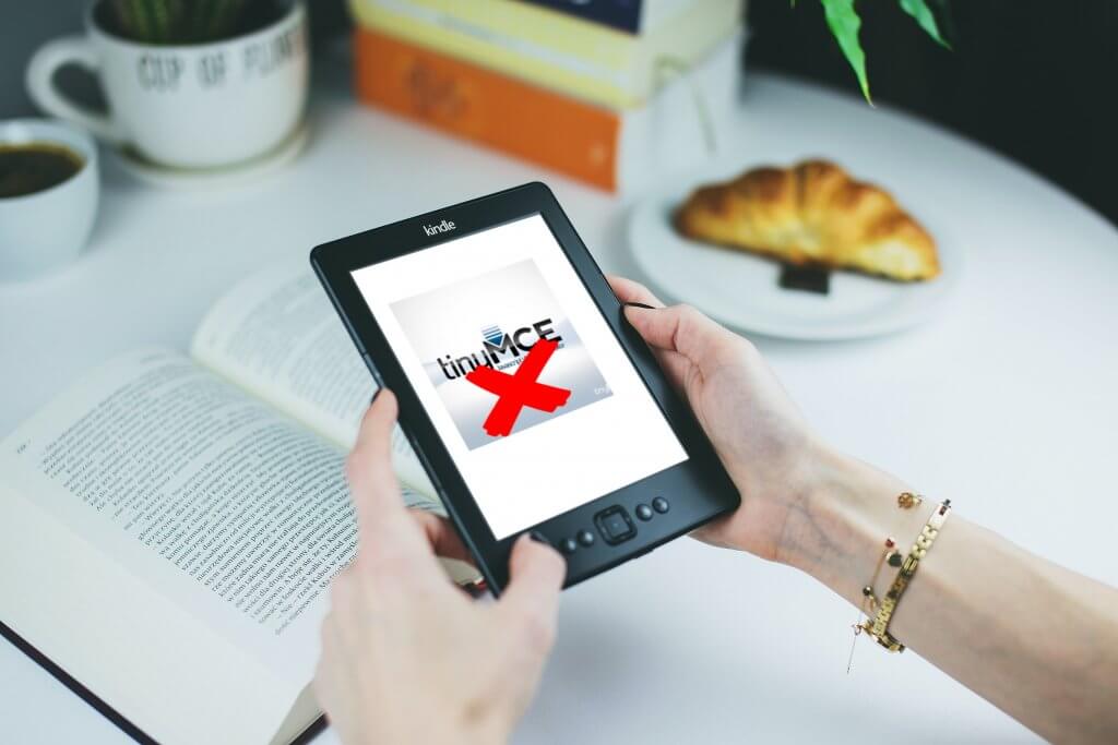 A person holding a tablet displaying a crossed-out TinyMCE logo.